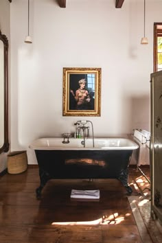 an old fashioned bathtub is in the middle of a wood floored bathroom with a painting on the wall