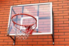 a basketball hoop hanging from the side of a brick wall with a window behind it