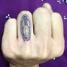 a person's hand with a small tattoo on the middle finger and an image of a virgin mary