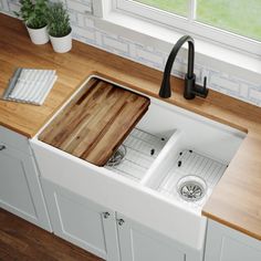 a white kitchen sink sitting under a window next to a wooden cutting board on top of a counter