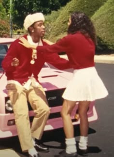 a man and woman sitting on the hood of a pink car