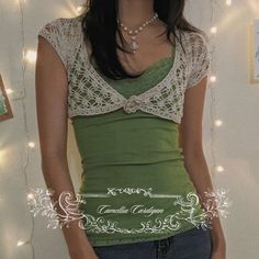 a woman wearing a green top with white lace on the neck and sleeves, standing in front of a string of lights