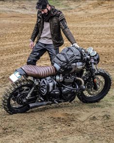 a man standing next to a parked motorcycle in the middle of a dirt field,