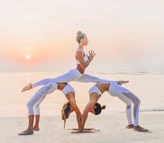 two women doing yoga poses on the beach at sunset with their hands in the air