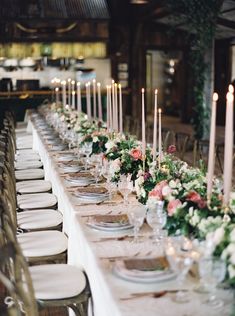 a long table is set with white and pink flowers, candles, and place settings