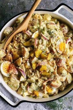 a bowl filled with potato salad next to a wooden spoon