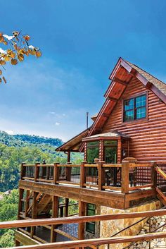 a log cabin with deck and railings on top of a hill overlooking the mountains