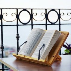 an open book sitting on top of a wooden table next to a metal balcony railing