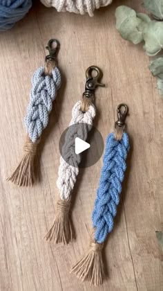 three different key chains on top of a wooden table next to some leaves and yarn