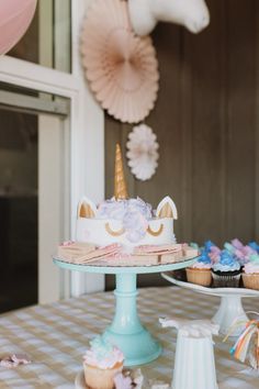 a table topped with cupcakes covered in frosting and unicorn hats hanging from the ceiling