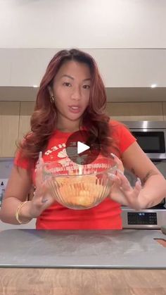 a woman in a red shirt is holding a bowl with food on it and standing next to an oven