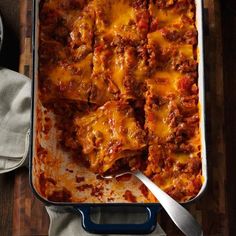 a casserole dish with meat and cheese in it on a wooden table next to silverware