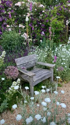 a wooden bench sitting in the middle of a garden filled with purple and white flowers