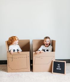 two children sitting in cardboard boxes on the floor