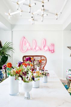 two photos of the same room with flowers in vases on the table, and an open neon sign above it