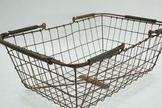 an old metal basket with two handles on the side and one in the middle, sitting on a white surface