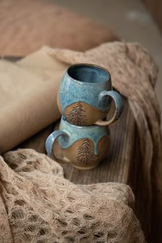 two mugs sitting on top of a wooden table next to a piece of cloth