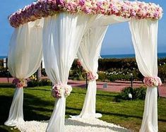 an outdoor wedding setup with white drapes and pink flowers on the canopy over it