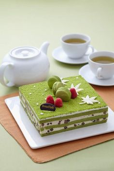 a piece of green cake with raspberries on it and two cups of coffee