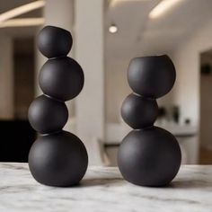 two black vases sitting on top of a marble table in front of a living room