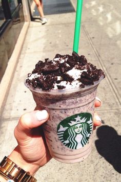 a person holding up a starbucks drink with oreo cookies and cream in it on the sidewalk