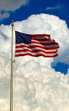 an american flag flying high in the sky with clouds behind it and blue skies above