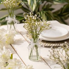 white flowers in vases on a table with plates and place settings for dinner guests