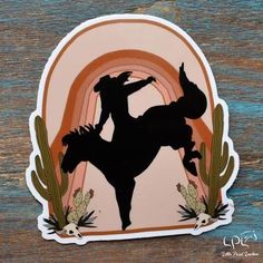 a sticker depicting a cowboy riding a horse with cactus and rainbow in the background