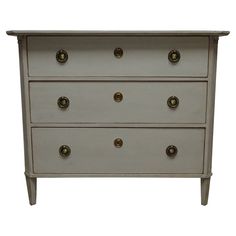 a white dresser with brass knobs on the top and bottom drawers, against a white background