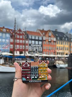 a person holding up a small piece of art in front of some buildings and water