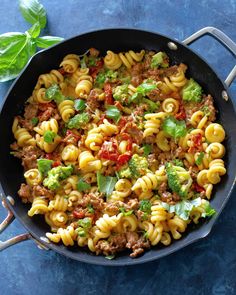 a skillet filled with pasta, meat and broccoli on top of a blue surface