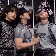 three young men standing next to each other in front of a wall with posters on it