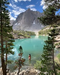 a woman standing on the edge of a mountain looking at a blue lake with snow capped mountains in the background