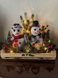 two snowmen sitting on top of a wooden box filled with christmas trees and lights