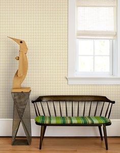 a bench sitting in front of a window next to a wooden bird on top of a stand