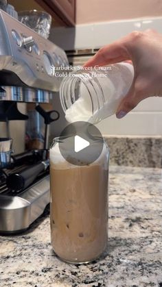 someone is pouring milk into a glass jar on the counter top in front of an espresso machine