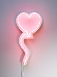 a pink heart shaped neon sign hanging from the side of a wall next to a phone