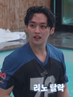 a young man standing in front of a swimming pool wearing a black and blue shirt