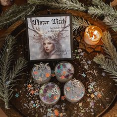 a wooden table topped with three candles and two containers filled with glittery decorations next to a book