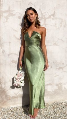 a woman in a green dress standing next to a wall holding a white flower bouquet