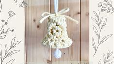 a crocheted bell ornament hanging on a wooden wall with flowers in the background