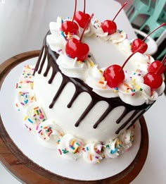 a cake with white frosting and sprinkles has cherries on top