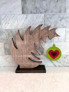 a wooden sculpture with a heart hanging from it's side next to a tile wall