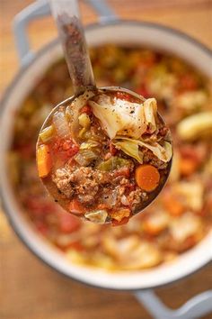 a spoon full of soup with meat, vegetables and potatoes in it on a wooden table