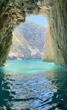 the inside of a cave with water and mountains in the background