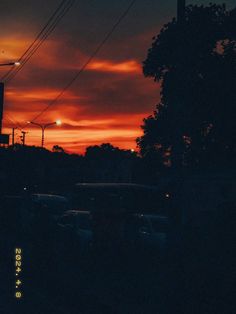 the sun is setting behind some power lines and cars parked on the side of the road