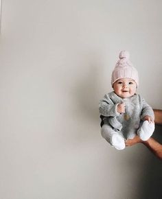 a man holding a baby wearing a pink hat and grey sweater while standing next to a white wall