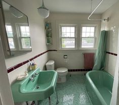 a bathroom with a green sink and bathtub next to a toilet under a window