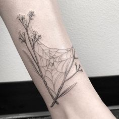 a spider web tattoo on the foot of a woman's leg with flowers and leaves