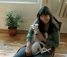 a woman sitting on a chair holding two dogs in her lap and smiling at the camera